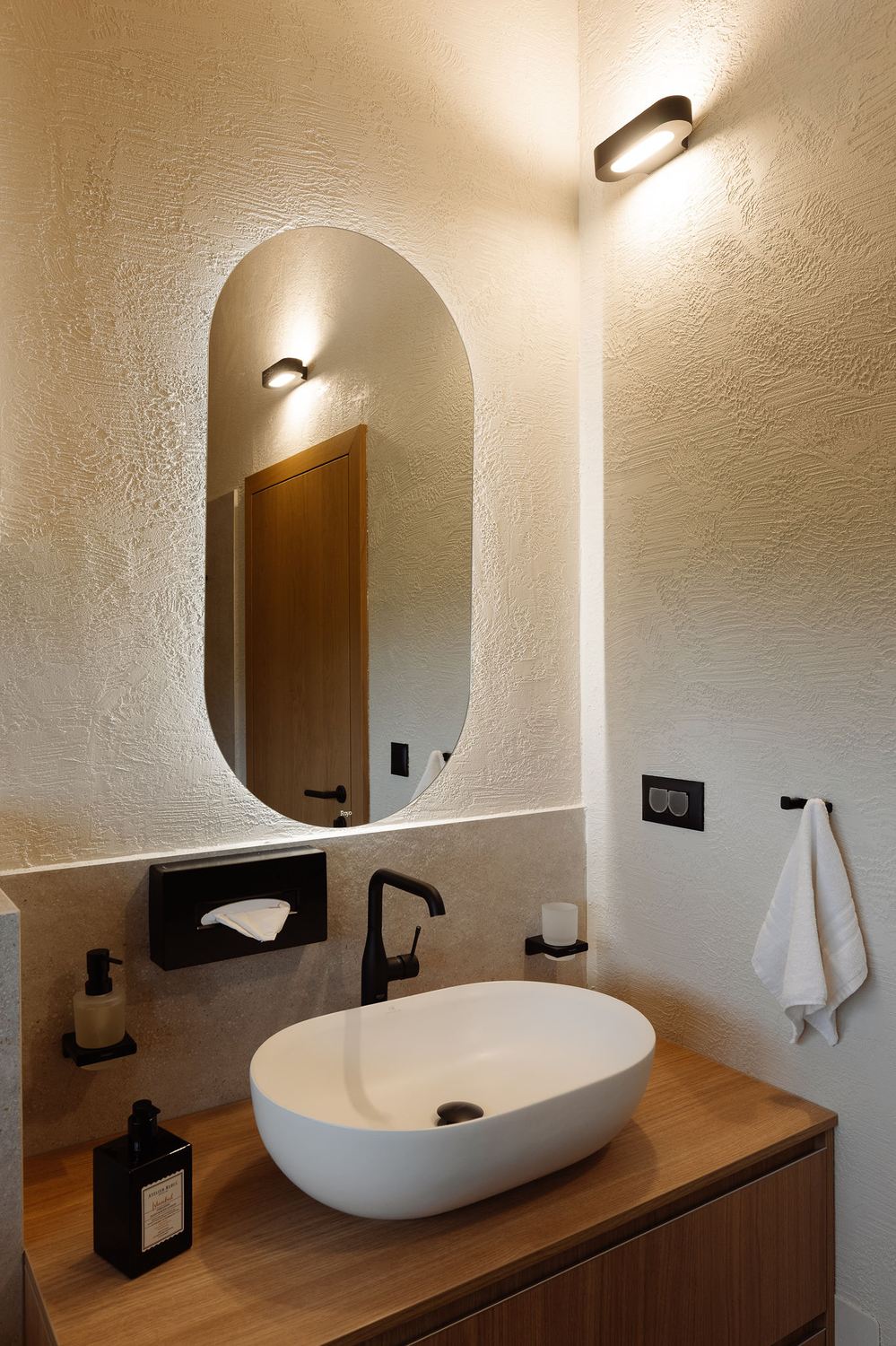 Bathroom with an oval mirror, dark tapware and a freestanding basin