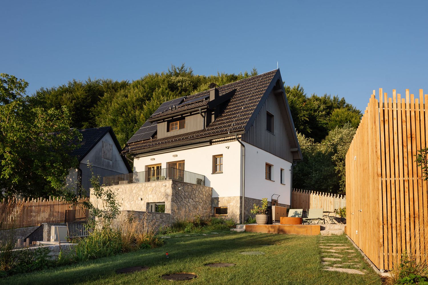 Endem House exterior with white render, dark timber gable and a wooden slat fence in golden evening light