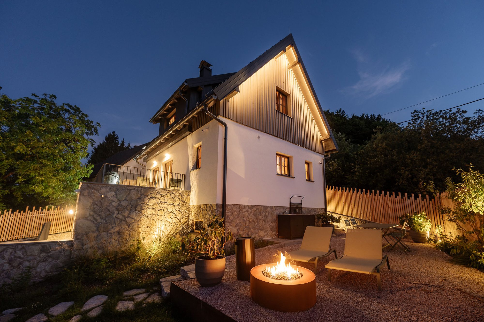 Endem House glowing at dusk, with a fire pit and lounge seating on the stone patio, forests of Plitvice behind